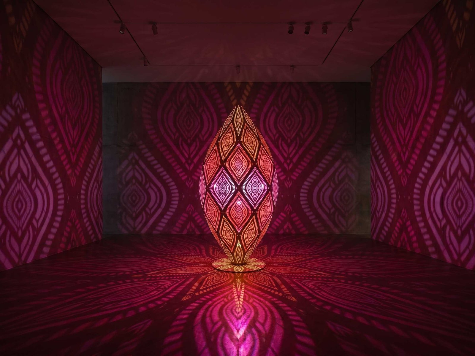 Large crimson teardrop metal light sculpture casting intricate pink and magenta lattice patterns on floor and walls